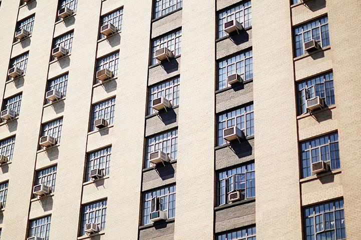 tan apartment building with air conditioning units coming out of most windows
