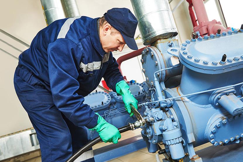 man in blue using wrench on hose attached to machinery