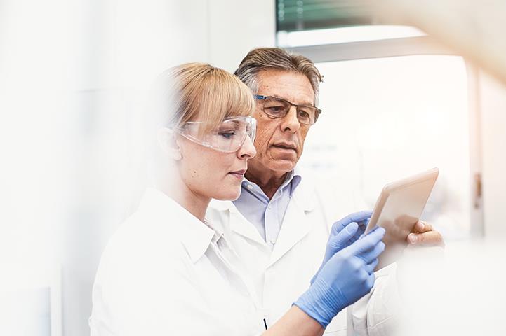 man and woman in lab coats looking at a smart tablet