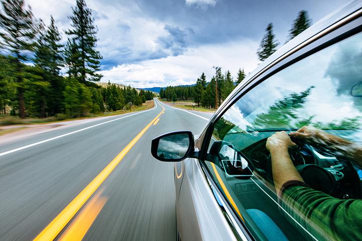 right side view of person driving on a road trees blurred on left side to indicate speed